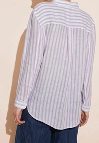 Camicia a maniche lunghe in tessuto leggero a righe con tonalità di lavanda e bianco. Presenta un orlo arrotondato e dettagli con polsini abbottonati.