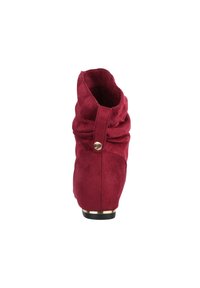 Rode suède enkellaars met geplooide details, gouden knoopaccent op de band en een lage zwarte hak met gouden rand, gezien vanuit de achterkant.