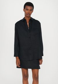 Black linen shirt with a collar, long sleeves, and a front pocket. The shirt features a subtle texture and a loose fit design.