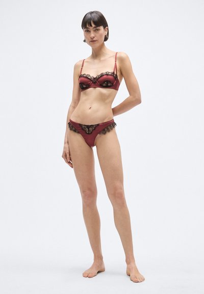 Set de lenjerie din satin roșu cu accente din dantelă neagră, sutien cu armătură și bretele reglabile, și tanga asortată cu margini din dantelă.