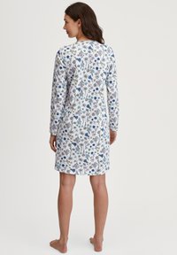 Vestaglia bianca a maniche lunghe con un motivo floreale nei colori blu, viola e giallo. Tessuto morbido, design alla ginocchia, orlo arrotondato.