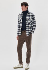Langärmliges kariertes Hemd in Weiß, Blau und Braun über einem marineblauen Rollkragenpullover, kombiniert mit braunen Cordhosen und weißen Sneakers mit grünen Akzenten.
