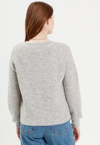 Grå strikket sweater med ribbet tekstur, raglanærmer og rund hals, båret med blå højtaljede jeans.