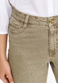 Beżowe dżinsy o dopasowanej sylwetce, z zamknięciem na górny guzik, przednimi kieszeniami na biodrach i subtelną teksturą.