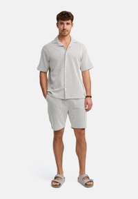 Kortærmet skjorte med knapper og matchende shorts i lys grå med hvide striber; parret med grå sandaler med justerbare remme.