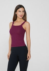 Bordeauxfarbenes, geripptes Tanktop mit breiten Trägern, tailliertem Design und quadratischem Ausschnitt. Kombiniert mit schmalen schwarzen Hosen. Keine sichtbaren Muster oder Akzente.