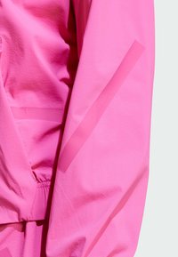Chaqueta de color rosa brillante con tejido texturizado, cintura elástica y rayas mate diagonales a lo largo de la manga para un detalle adicional.