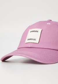Roosa puuvillane baseballi müts, millel on esiküljel ristkülikukujuline valge patch, kus on "SAM SØE" bränding, kõver ääre ja broderitud detailid.