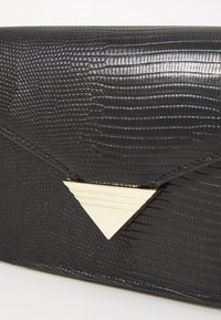 Pochette en simili cuir noir texturé avec un accent triangulaire métallique et un design d'enveloppe épuré, présentant des motifs embossés sur la surface.