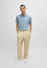 Lys blå polo skjorte med krave og hvid kant, parret med beige plisserede bukser og hvide sneakers. Enkel design, casual look.