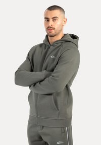 Grå zip-hoodie lavet af blødt stof, med kengurulommer, ribbede manchetter og et lille logo på brystet. Simpelt design.