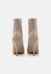 Bottes cheville en maille beige avec un design ajusté, un talon haut effilé et une texture lisse. Présentent un revers côtelé et une couture arrière sans couture.