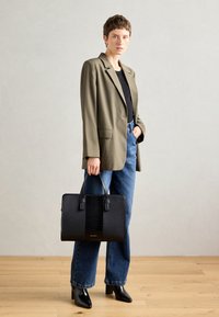 Sac à main en cuir noir avec finition brillante et panneau central texturé. Accompagné d'un blazer gris et d'un jean taille haute bleu.