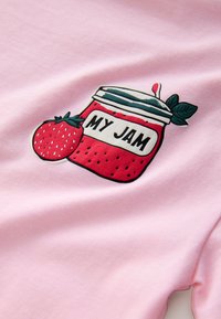 Rosa tyg har en grafik av en burk märkt "MY JAM" med en jordgubbe och gröna blad, konturerade i svart för kontrast.