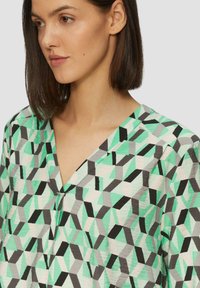 Geometrisch patroontop met mintgroene, zwarte en grijze tinten; lichte stof met een v-hals en een relaxte pasvorm.
