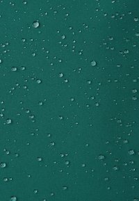 Gouttes d'eau de tailles variées dispersées sur une surface textile lisse de couleur vert foncé, montrant une répulsion de l'eau.