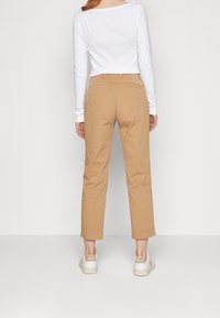 Pantalon en coton beige avec une coupe droite, ourlé au niveau de la cheville. Associé à un haut à manches longues blanc et des baskets blanches avec des accents de logo.