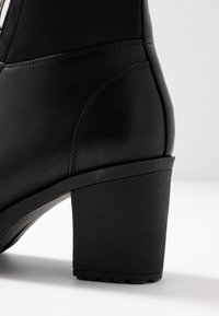 Schwarzer Absatzstiefelette aus strukturiertem Synthetikmaterial. Verfügt über eine abgerundete Zehenpartie, einen Blockabsatz und gestickte Akzente entlang des Schafts.