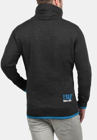 Pull noir gris avec un col montant, doté d'accents bleus aux poignets et à l'ourlet. L'arrière comprend un logo et le texte "Depuis 1993". Texture douce.