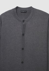 Cardigan grigio realizzato in morbido tessuto a maglia, con collo rotondo, chiusura frontale con bottoni e cinque bottoni neri lungo la patta.
