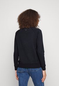 Sweatshirt noir avec un ourlet et des poignets côtelés, présentant des manches raglan et un petit détail de logo à l'arrière du col.