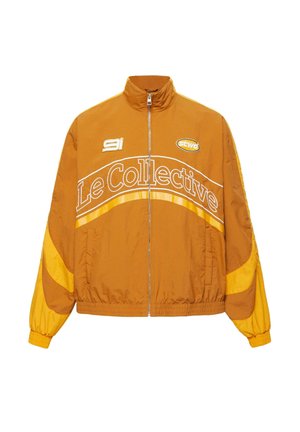 Sennepsgul lynlåstrøje med elastiske manchetter, hvid "Le Collective" tekst på brystet og små logoer nær kraven på en hvid baggrund.
