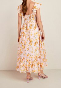 Květinové maxi šaty s volánovými rukávy, nařaseným korzetem v světle růžové barvě s žlutými květy a splývavou sukní v několika vrstvách. Noseny s levandulovými sandály.