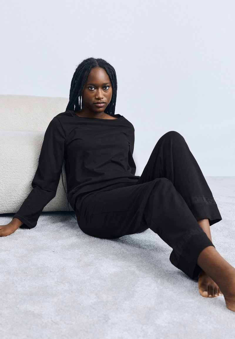 Črno dolgo majico z dolgimi rokavi in ujemajoče hlače iz mehke tkanine. Ohlapen kroj s širokim izrezom. Gladek tekstura, minimalističen dizajn.