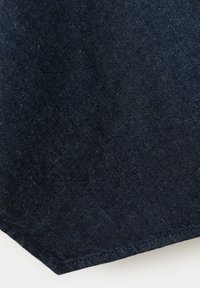 Gros plan d'un tissu denim bleu foncé avec une texture de tissage visible et un ourlet cousu sur fond blanc.