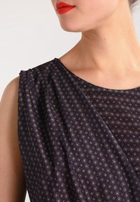 Marinblå klänning med blommönster, mjuk textur, draperad detalj på axeln, rund halsringning och korta ärmar.