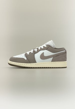 Zapatilla de perfil bajo con piel blanca y paneles de ante gris, cordones blancos, entresuela beige claro y el logo de Nike sobre un fondo neutro.