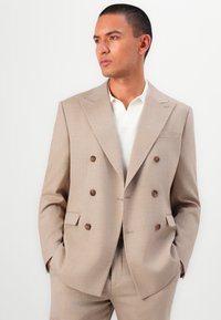 Light beige double-breasted blazer with brown buttons, notch lapels, and a subtle texture, paired with a white polo shirt.