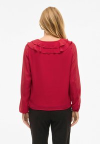 Camicia rossa con scollatura arricciata, maniche lunghe trasparenti e una texture liscia. La vista posteriore mostra una vestibilità rilassata e dettagli delle cuciture sottili.