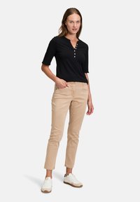 Černé krátké rukávy henley tričko s knoflíkovými detaily, kombinované se světle béžovými slim-fit kalhotami a bílými teniskami s hnědými akcenty.