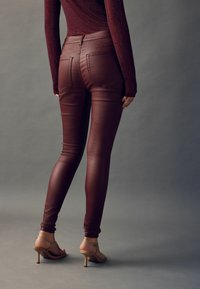 Bordeaux, fusk läder slim-fit byxor med hög midja, featuring två bakfickor och en slät, glänsande yta. Bärs med remsandaler.