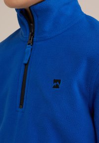 Pullover in fleece blu con colletto alto, zip frontale e accento logo nero. Texture morbida con una finitura liscia e senza motivi visibili.