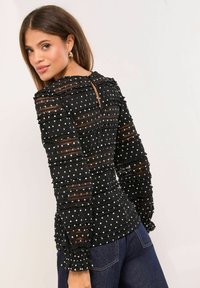 Mustblus tekstuurse kangaga, laskukeste ja valgete täppidega. Omab pikki varrukaid ja seljal avausteega lõiget.