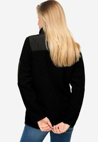 Svart fleece-pullover med ett kviltat svart axelparti och lång ärm. Mjuk textur, avslappnad passform och hög hals.