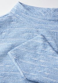 Hellblauer, strukturierter Stoff mit einem dezenten Streifenmuster, ausgestattet mit einem umgeschlagenen Kragen und Ärmelrand, der ein weiches, gewebtes Aussehen präsentiert.