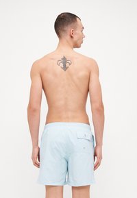 Lys blå badebukser med elastisk liv, med en baklomme med knappelukking. Glatt tekstur og knelengt design.