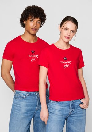 T-shirts en coton rouge à manches courtes, ornés du texte blanc "tommy girl" et d'un motif d'étoile. Portés avec un jean en denim bleu.