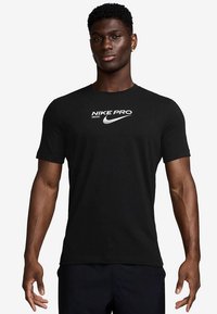 Must Nike Pro lühikeste varrukatega T-särk, valmistatud pehmest kangast, esiühel valge logo ja tekst, klassikalise ümara kaelusega.