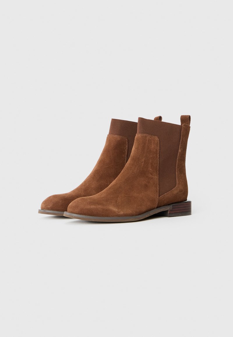 Braune Wildleder-Stiefeletten mit elastischen Seiteneinsätzen, abgerundeter Zehenpartie und niedrigem Blockabsatz. Glatte Textur ohne sichtbare Muster oder Beschläge.