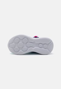 Schuhsohle aus weißem Gummimaterial mit sechseckigem Profil für besseren Halt, akzentuiert durch einen pinken Riemen und strukturierten Rillen.