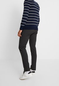 Námořnický pruhovaný pletený svetr s bílými pruhy, tmavě šedé kalhoty na míru a bílé tenisky s černými detaily. Důraz na moderní design a materiály.