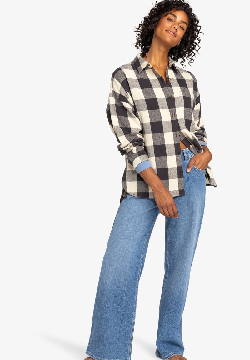 Black and cream checkered button-up shirt with rolled sleeves, paired with wide-leg blue denim jeans.