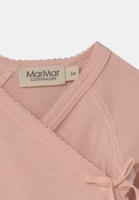 Rózsaszín pamut baba hátlap, ívelt szélekkel, szalaggal összekötve, és a "MarMar Copenhagen" felirattal ellátott címkével, mérete 50.
