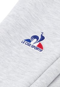 Gray sweatshirt fabric with a textured appearance, featuring an embroidered logo in blue, white, and red, reading "LE COQ SPORTIF."