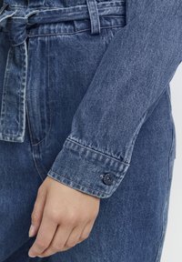 Farmereing ing, övvel megkötve, hosszú ujjú, gombos mandzsettával, világoskék színben. Feltűnő, texturált anyag, laza stílus.