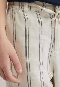 Linen hlače v kremni barvi z vertikalnimi črnimi črtami. Imajo elastičen pas in vrvico, ob strani pa je vidna žep.
